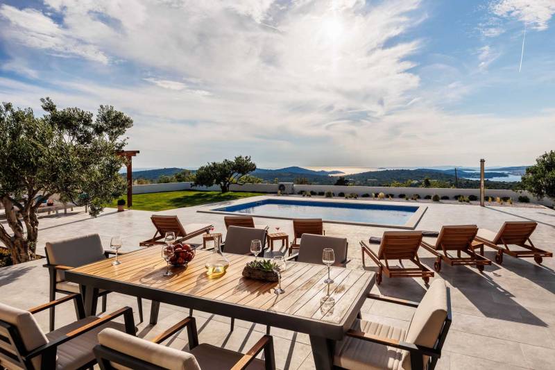 Villa Volare in the Primošten area with a private pool, sun loungers, and a dining table on a spacious terrace. Beautiful view of the sea and islands in the background.